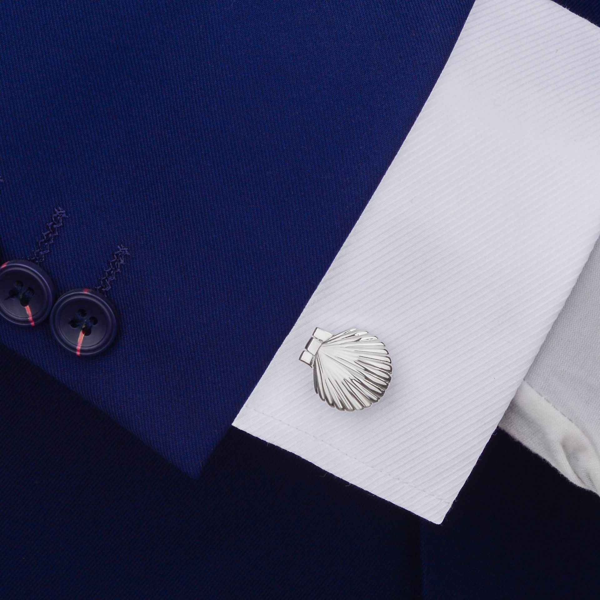 Silver-tone shell-shaped cufflinks on a shirt cuff, ridged scallop front