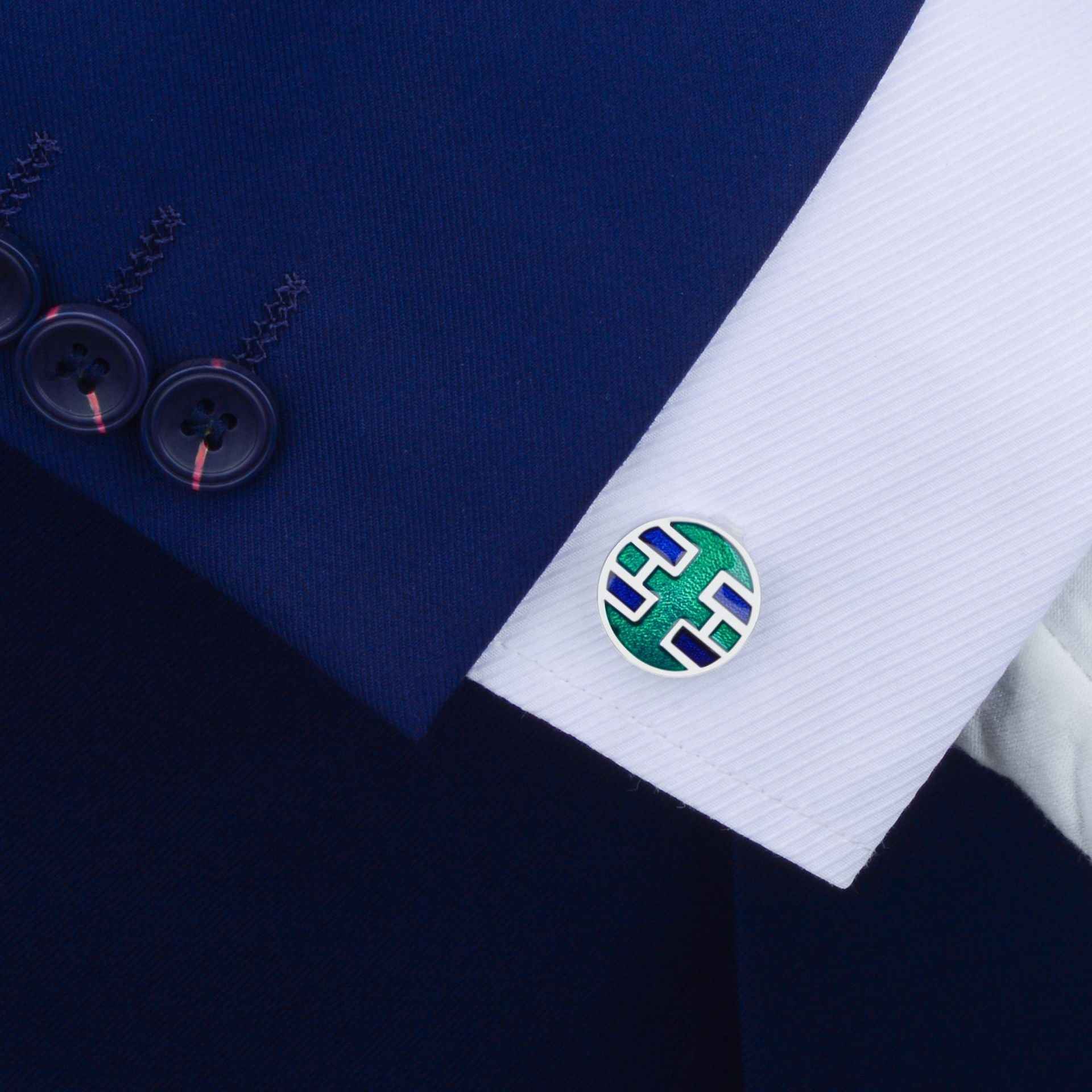 Round green cufflink with blue geometric enamel on white dress cuff