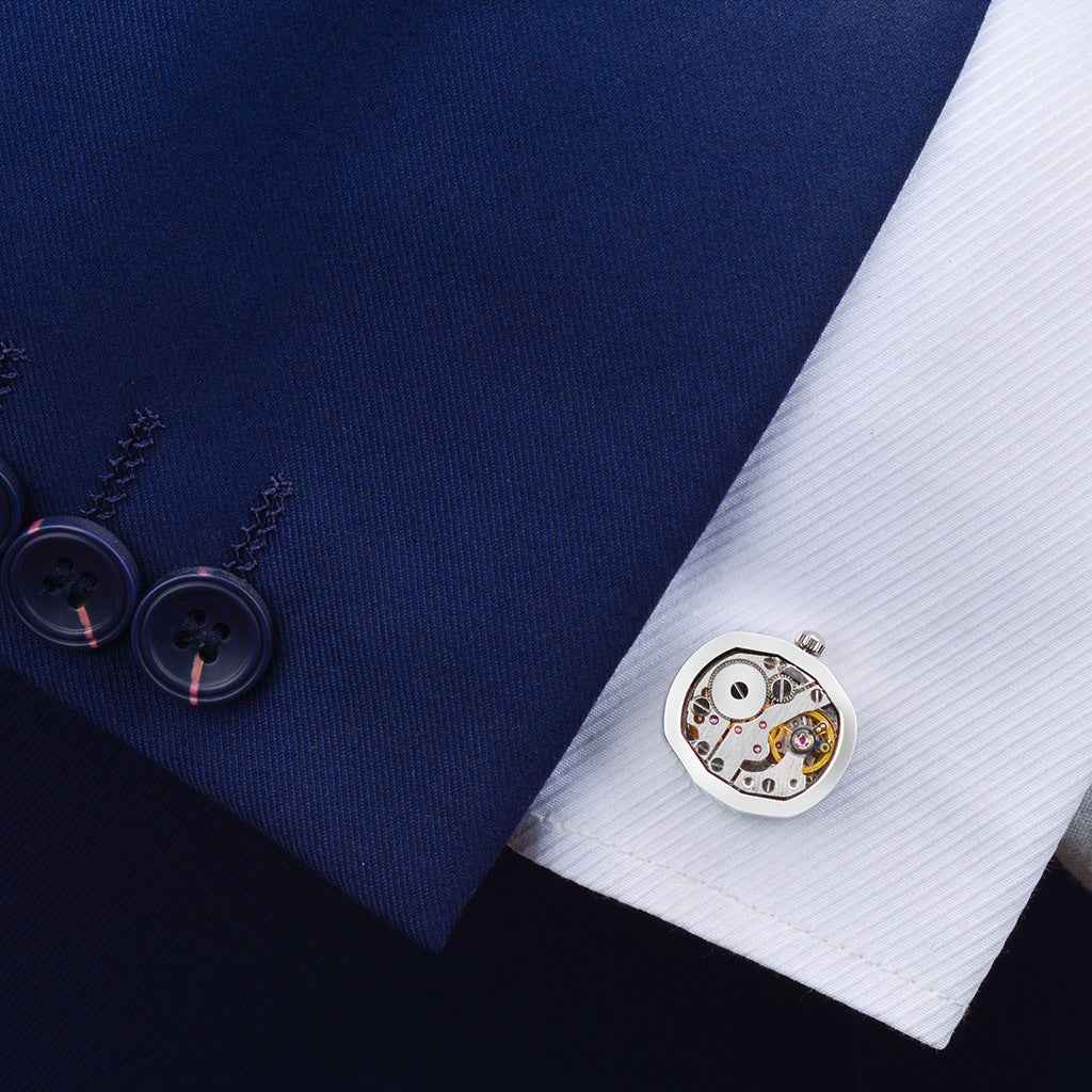 Gold mechanical watch movement cufflinks on a white dress shirt cuff, round dial visible