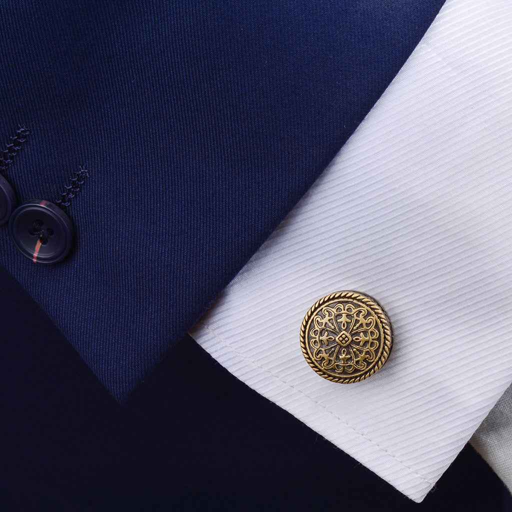 Antique bronze round cufflinks on white shirt cuff, engraved filigree center emblem