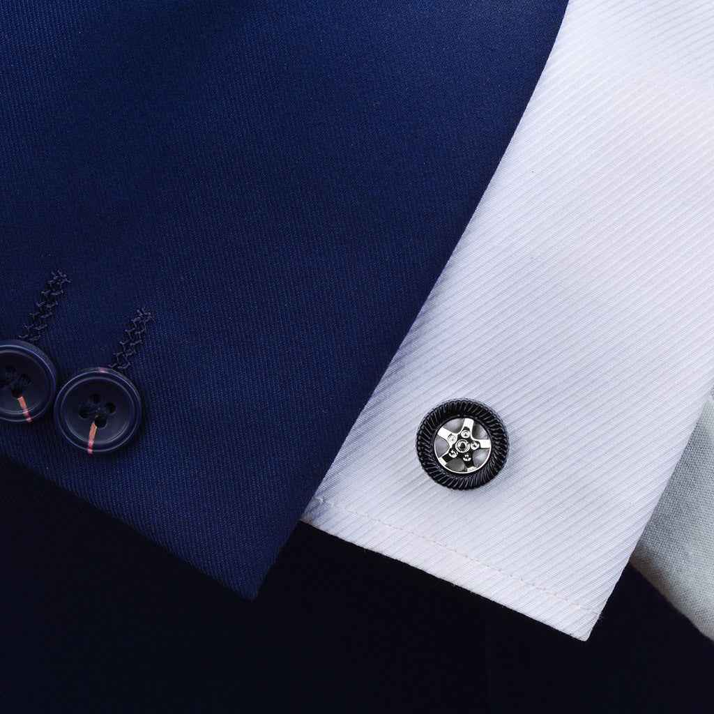 Black tire-shaped cufflink on shirt cuff with wheel hub detail