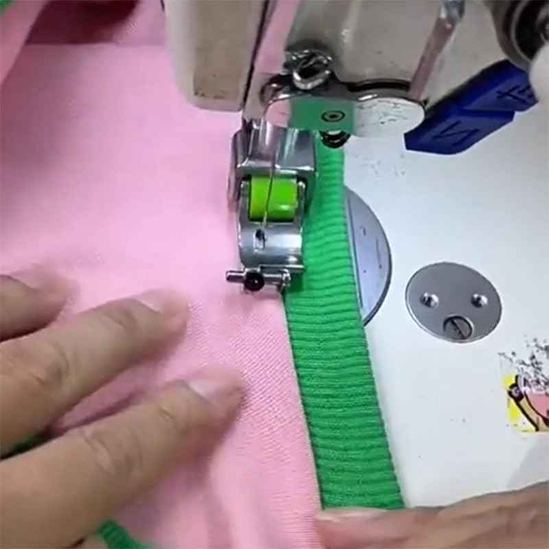 Presser foot sewing with green fabric trim guided along an edge on a pink textile