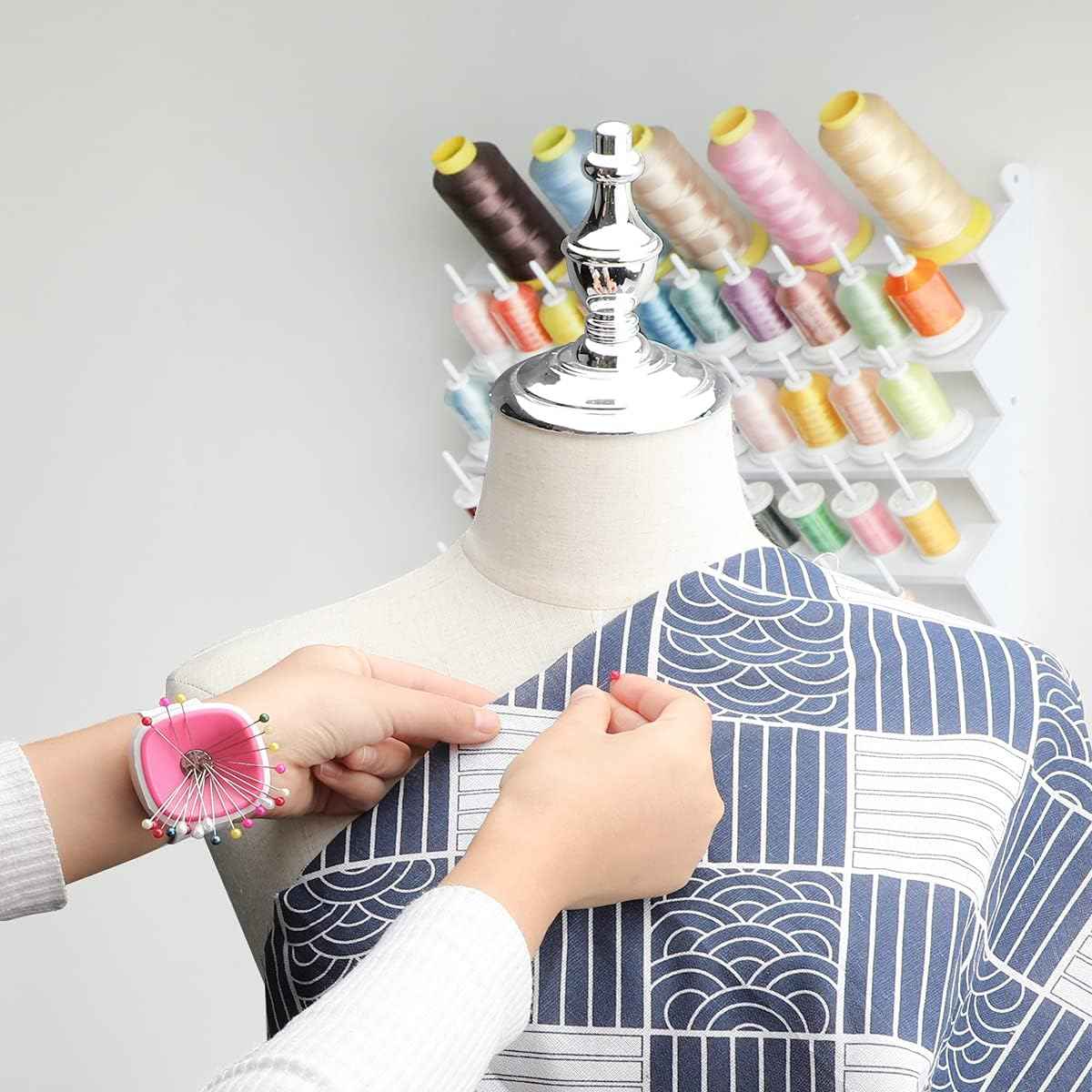 Pink magnetic wrist pin cushion on a mannequin wrist with sewing pins near the fabric.