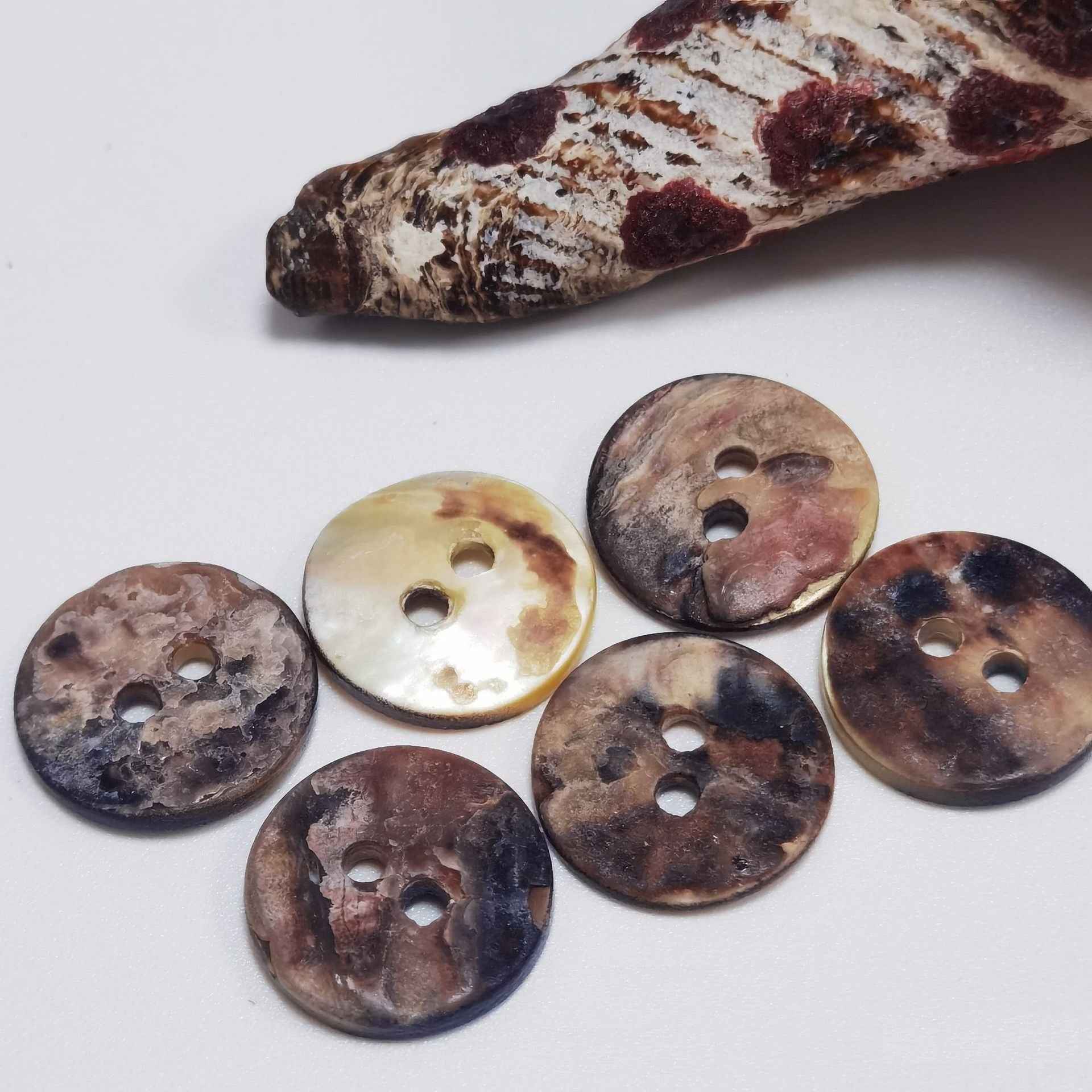 Assorted round mother-of-pearl 2-hole buttons, mottled shell colors, each with two holes.