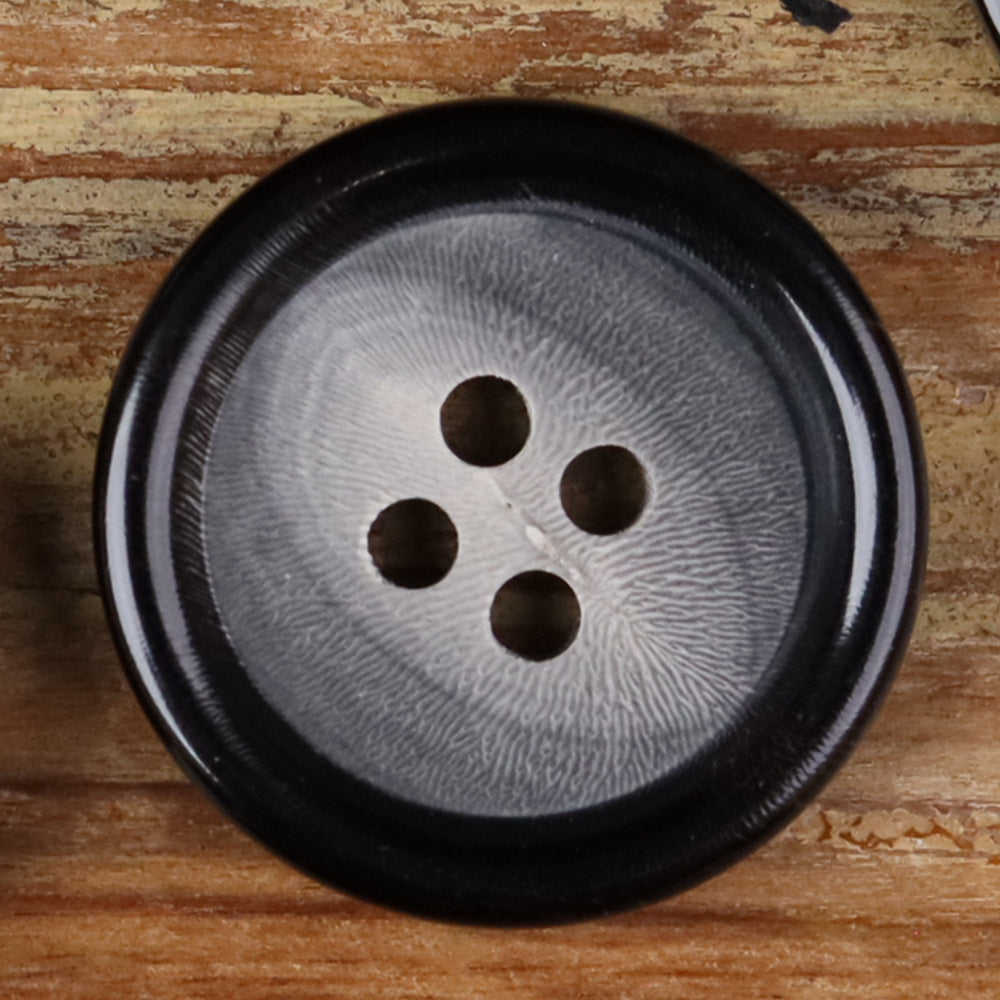 Close-up of a 4-hole round horn-style button with four holes on a dark face