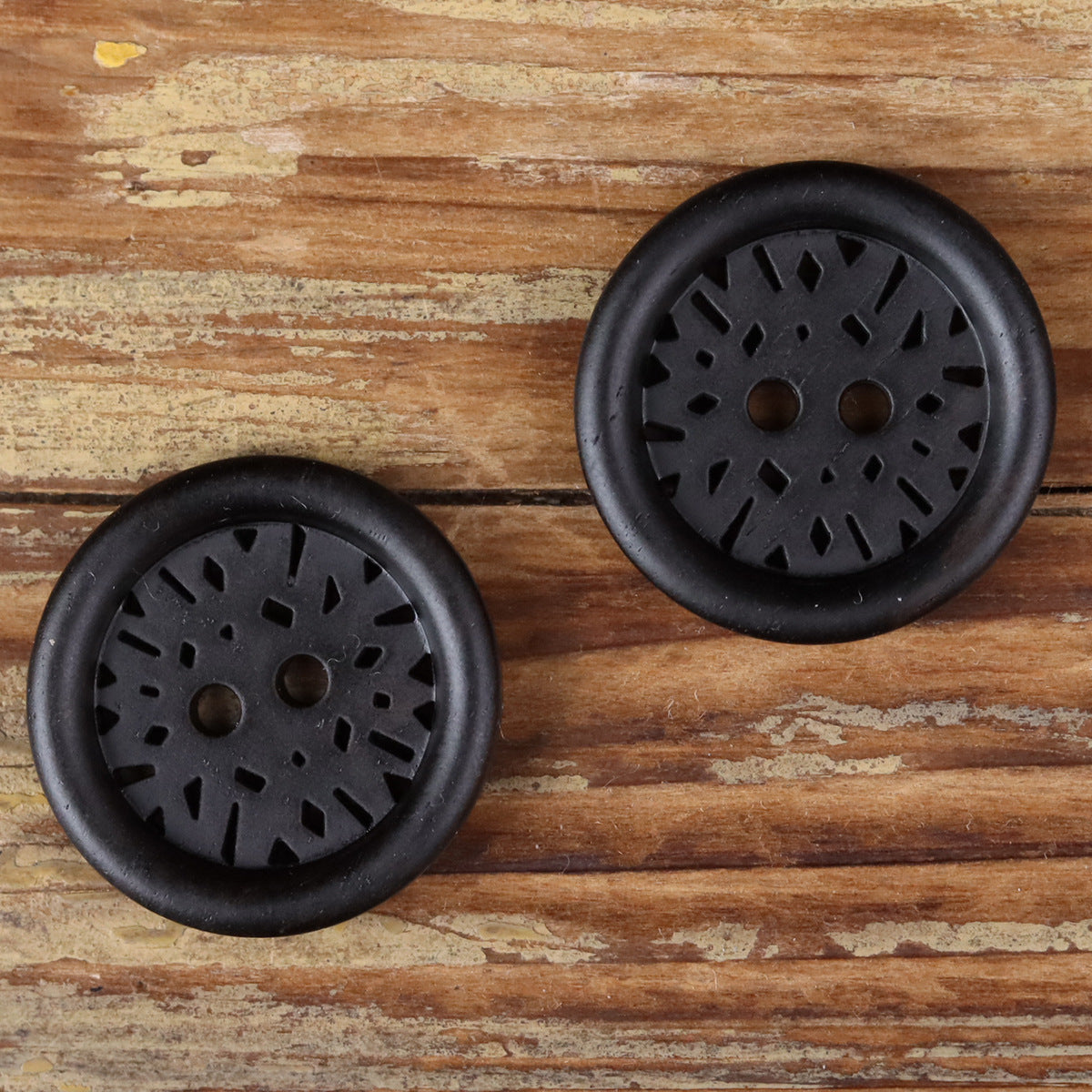 Two dark round 2-hole coat buttons with radial laser-cut design