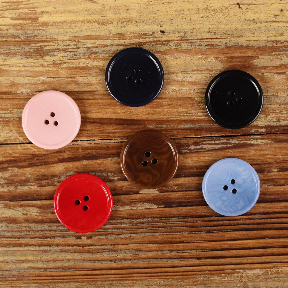 Round 3-hole buttons in pink, red, light blue, brown, navy, and black on wood