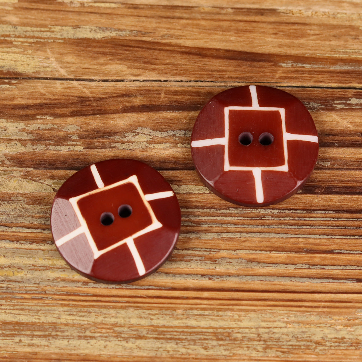 Pair of round red buffalo horn buttons with white cross markings and 2 holes