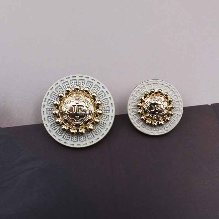 Gold-tone round metal shank button on white base, with central monogram design