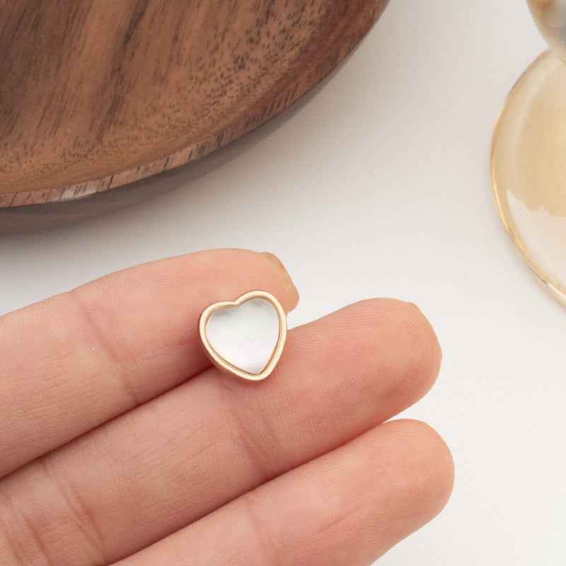 Heart-shaped button with white iridescent center and gold-tone border, close-up on hand