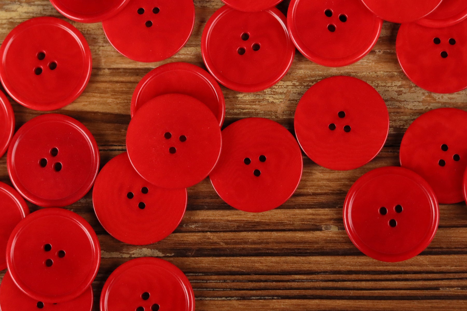 Assorted red round 3-hole buttons with thin rim on wood