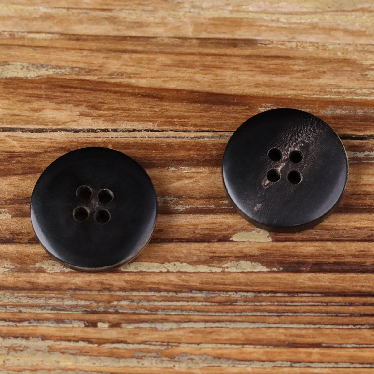 Two black 4-hole flat buttons with smooth matte surface and horn-grain finish