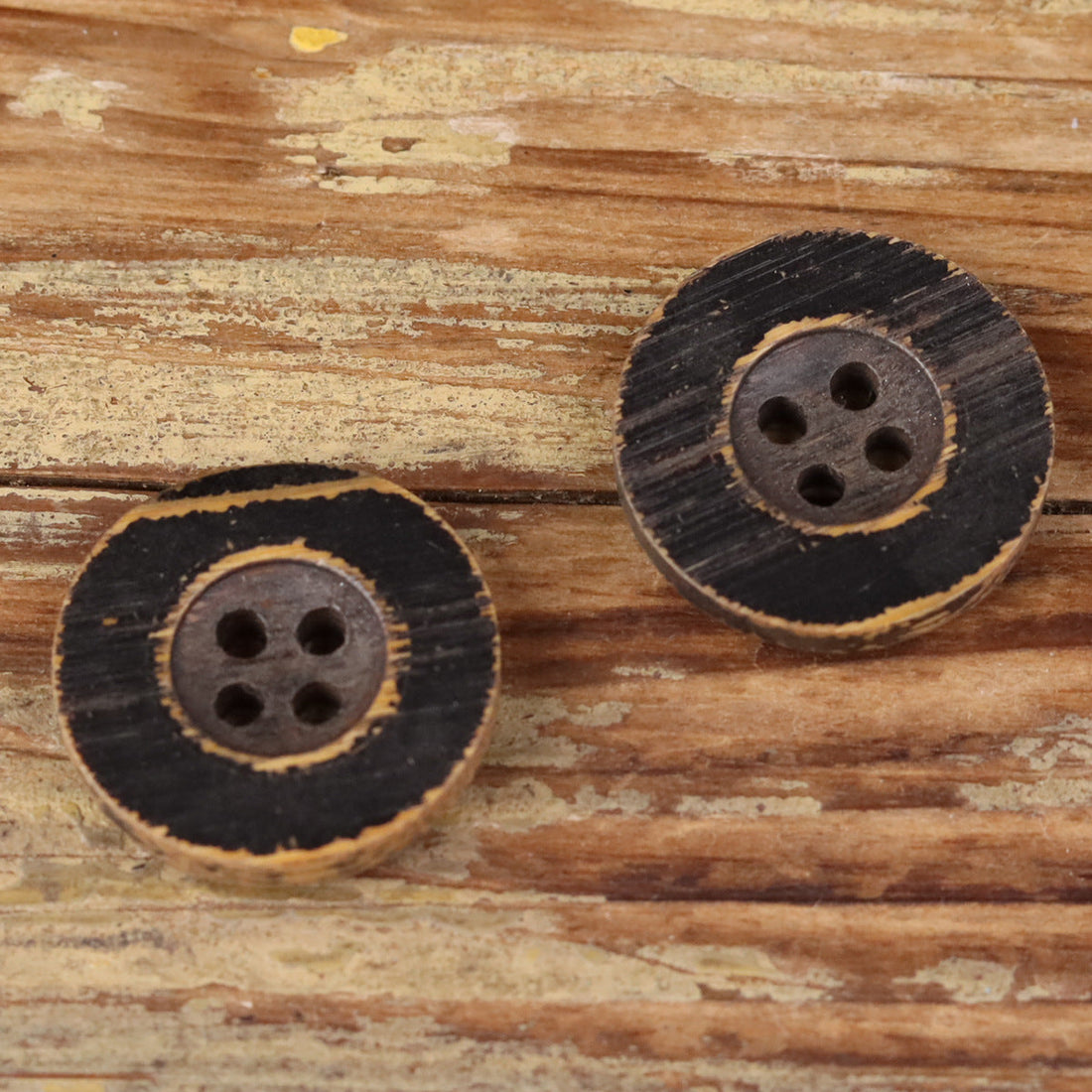 Round black distressed wood button with four holes, vintage style.