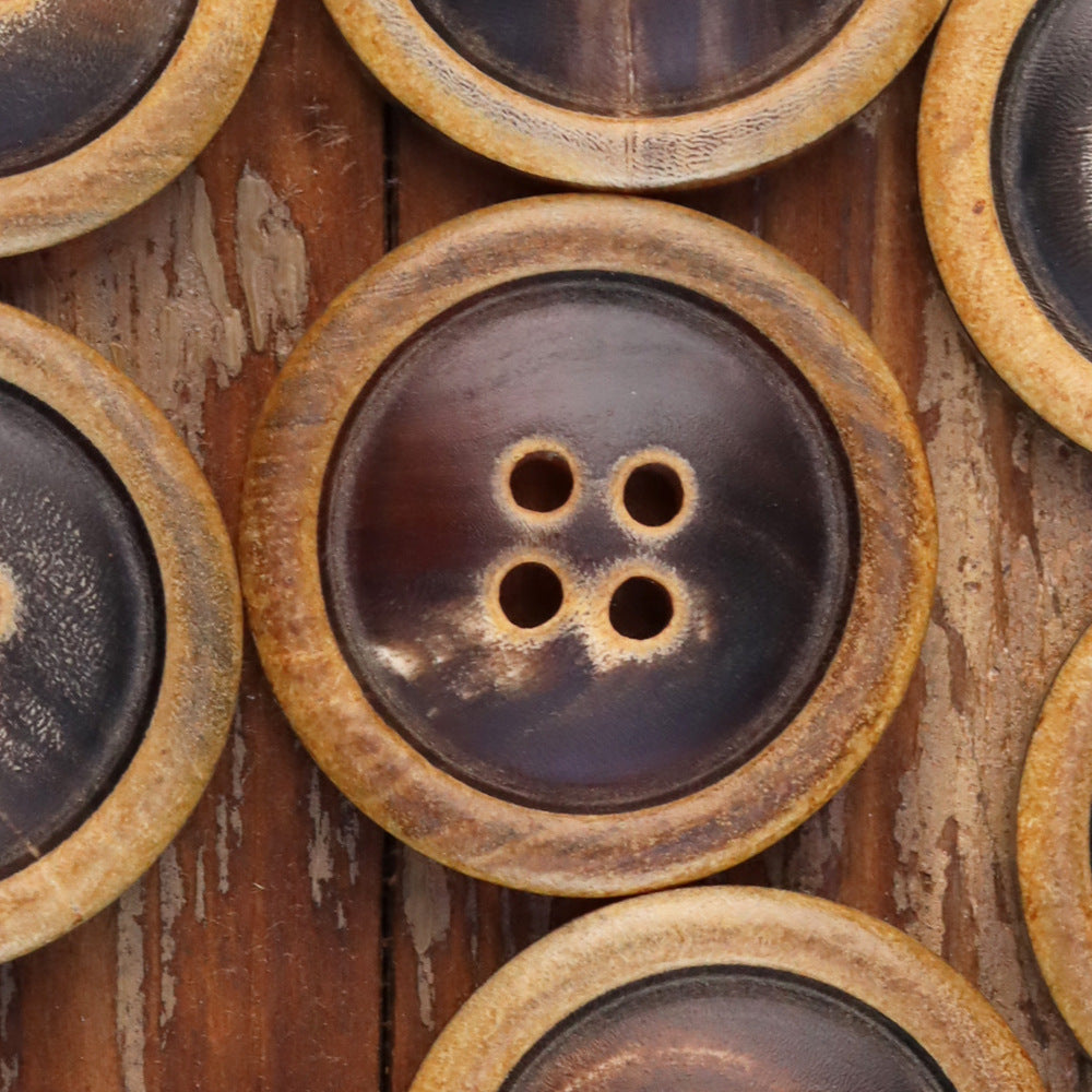 Close-up of round 4-hole coat button with dark face and tan burnished rim