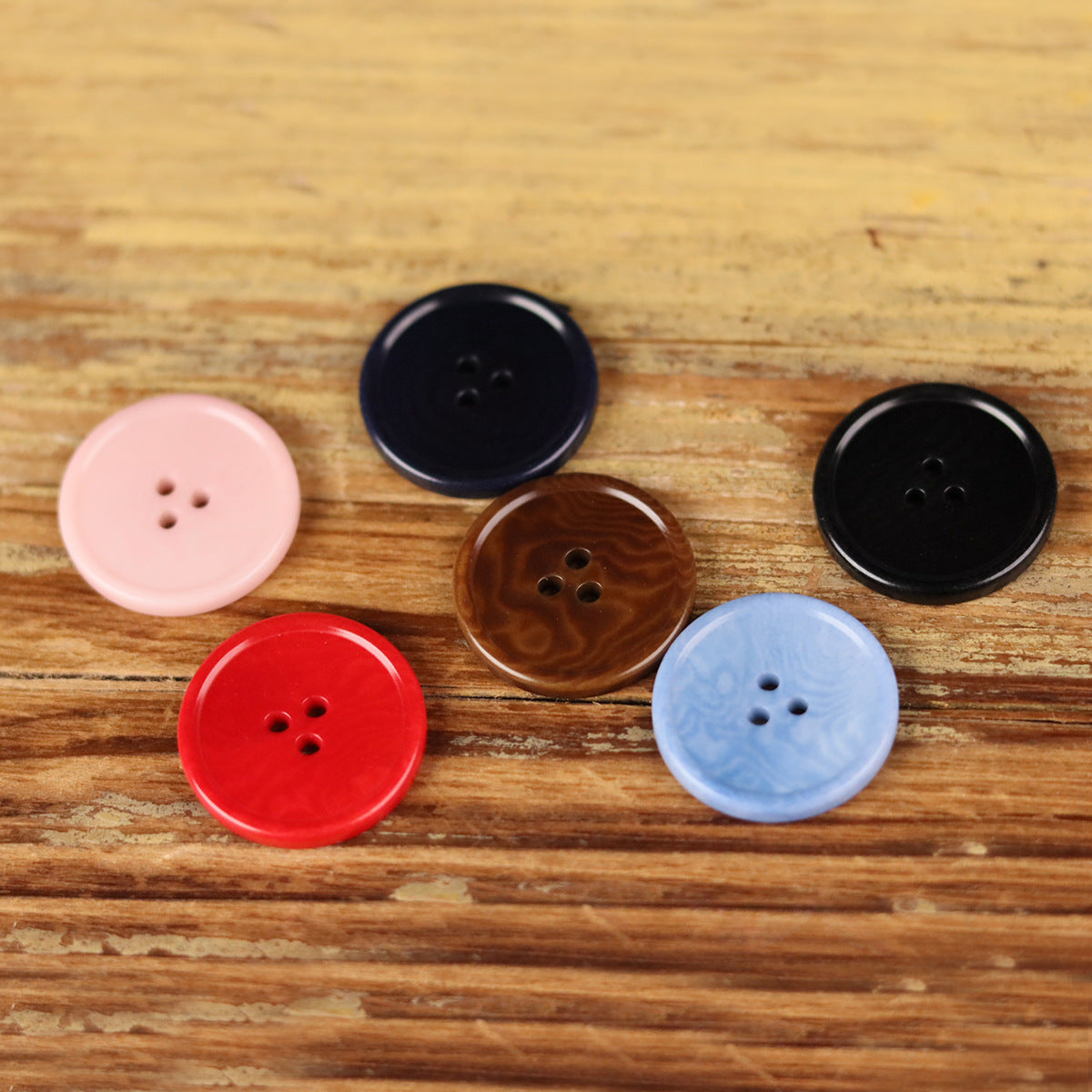 Round 3-hole buttons: light pink, red, light blue, brown, and black on wood