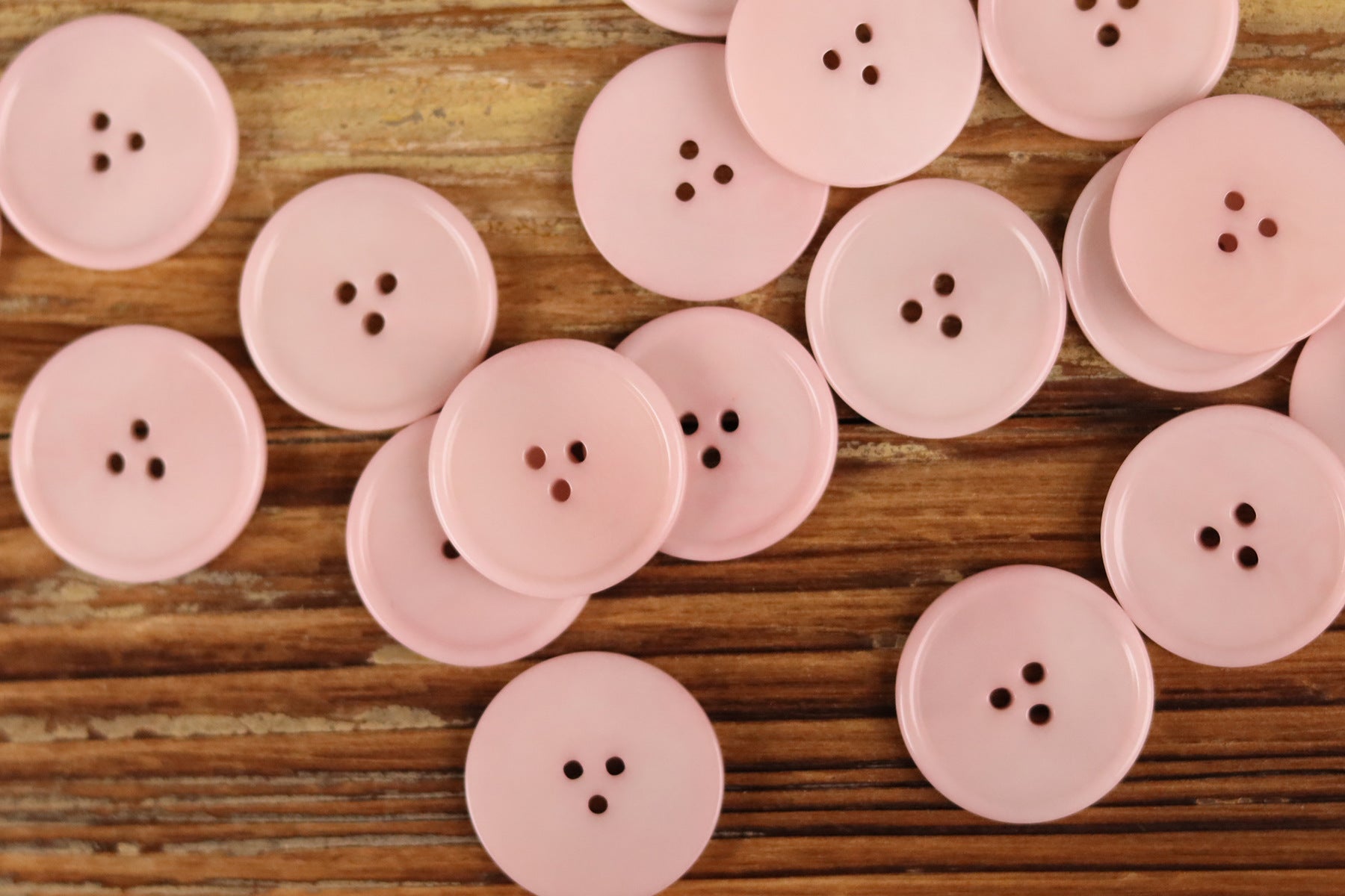 Assorted light pink round 3-hole buttons with thin rim on wood