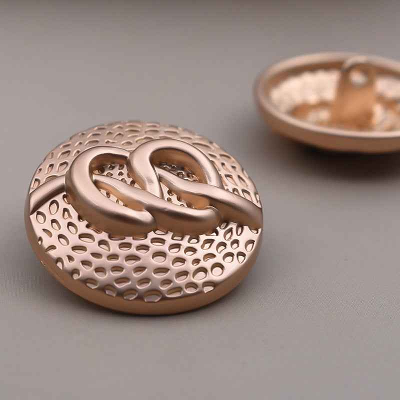 Round metal coat button with mottled dot texture and raised swirl detail, bronze