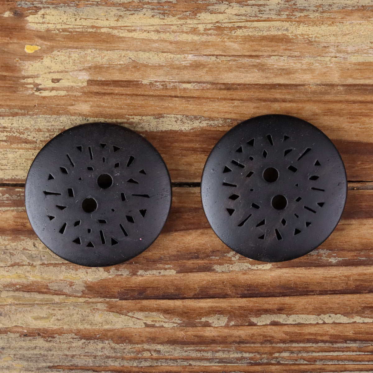 Round dark 2-hole coat button with laser-cut radial pattern, two shown