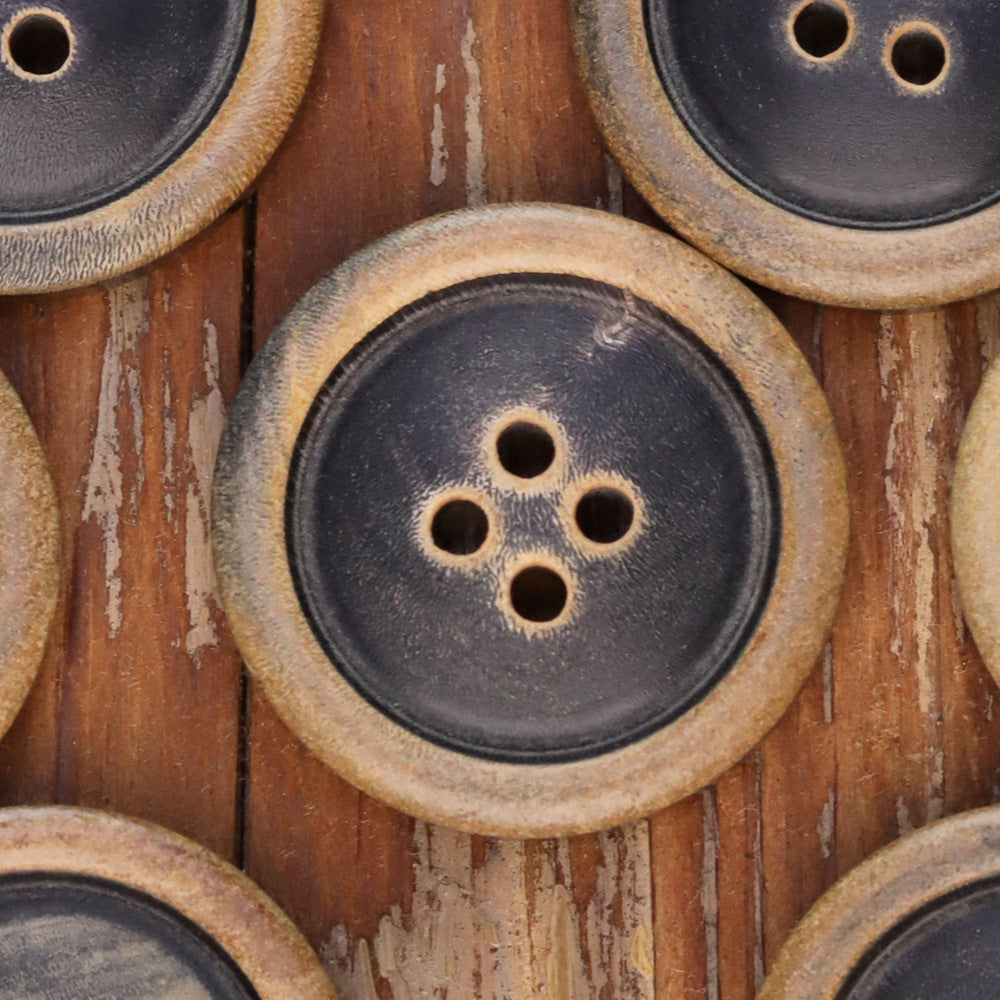 Close-up of round 4-hole coat button with dark face and tan burnished rim