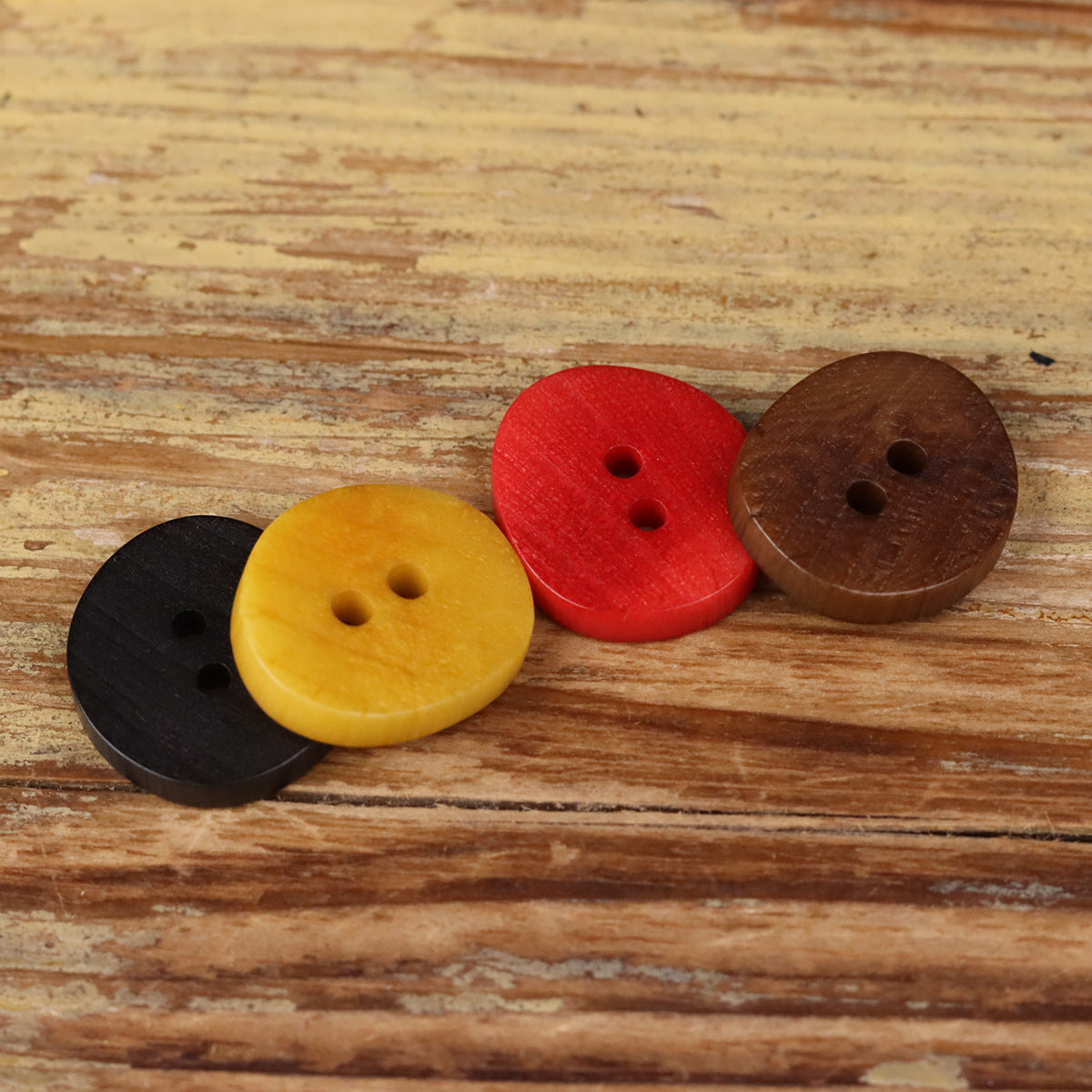 Set of natural 2-hole buttons in black, yellow, red, and brown, front view.