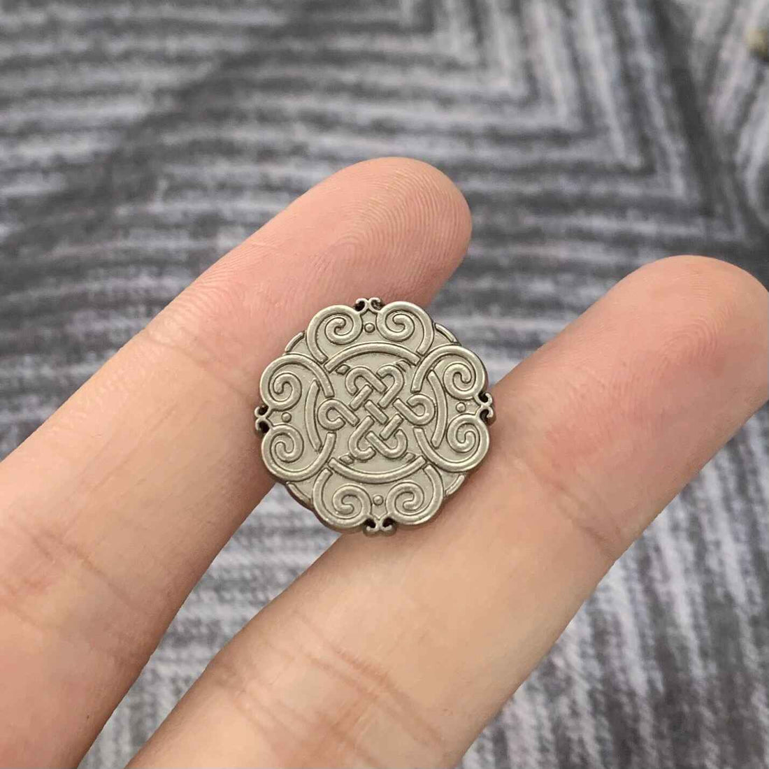 Matte silver Chinese knot motif metal button, round with raised swirl design.