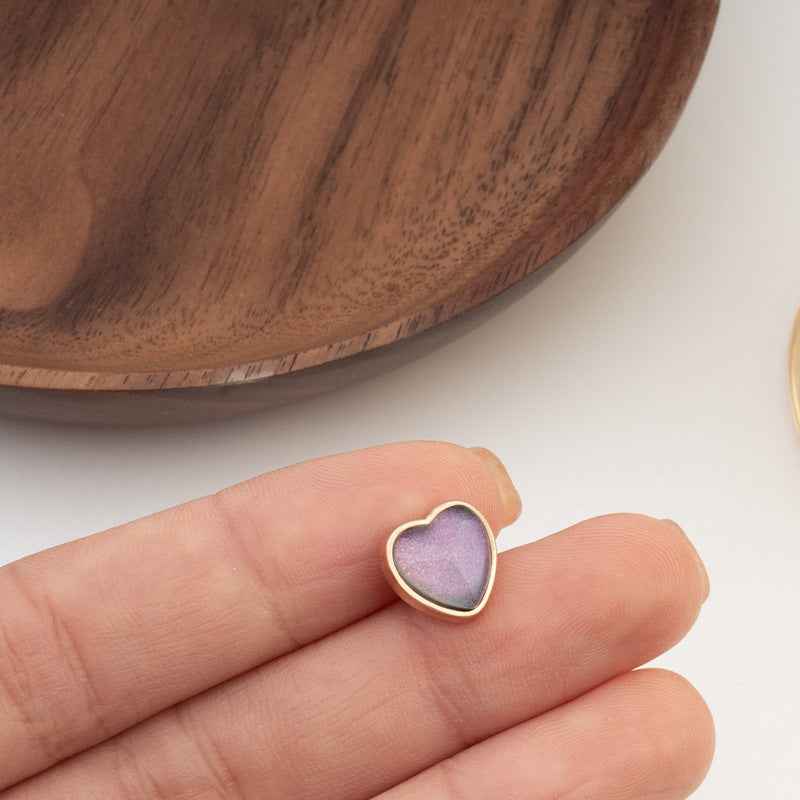 Heart-shaped button with lavender iridescent center and gold-tone edge, close-up on hand