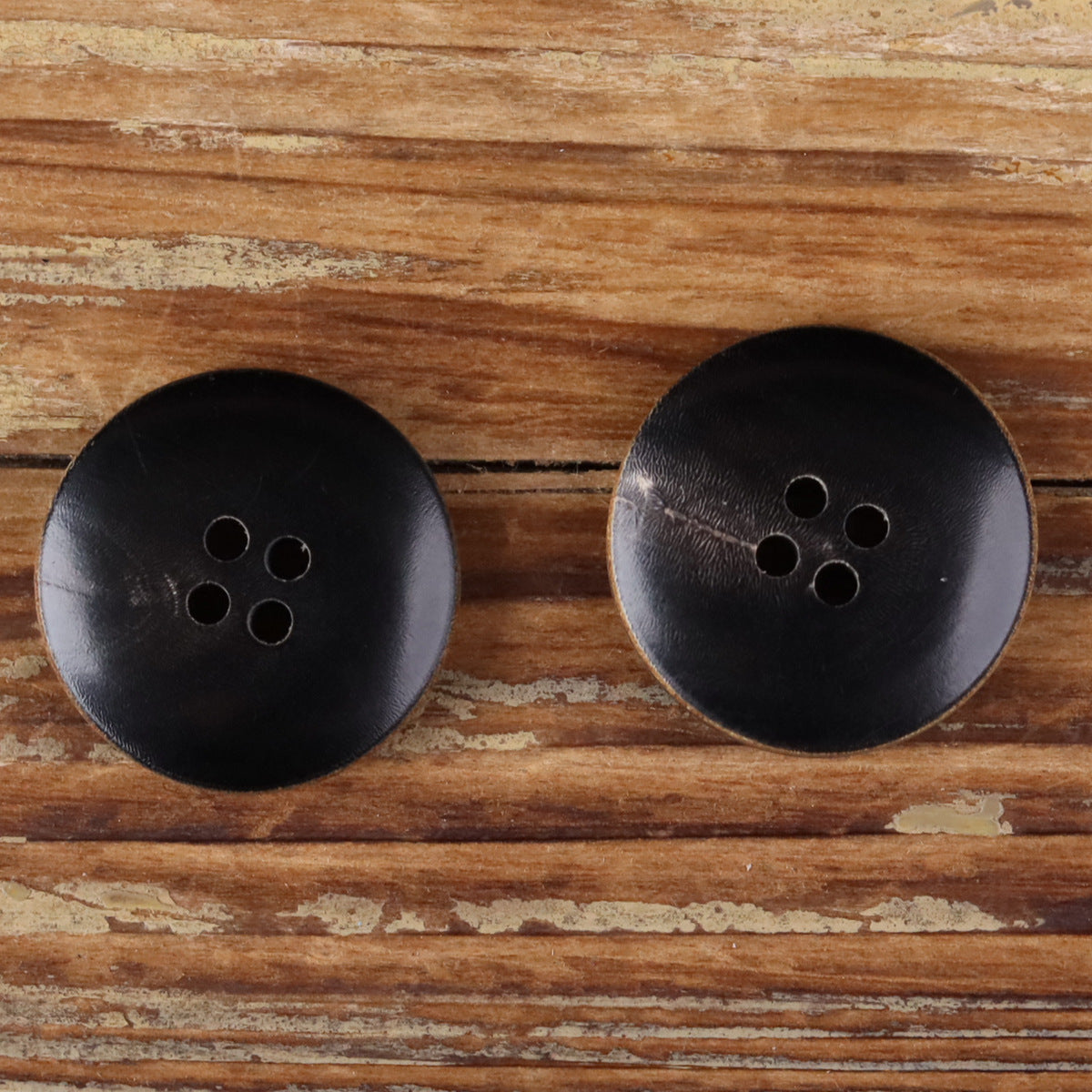 Pair of dark matte buffalo horn buttons with burnt edges and four-hole fronts