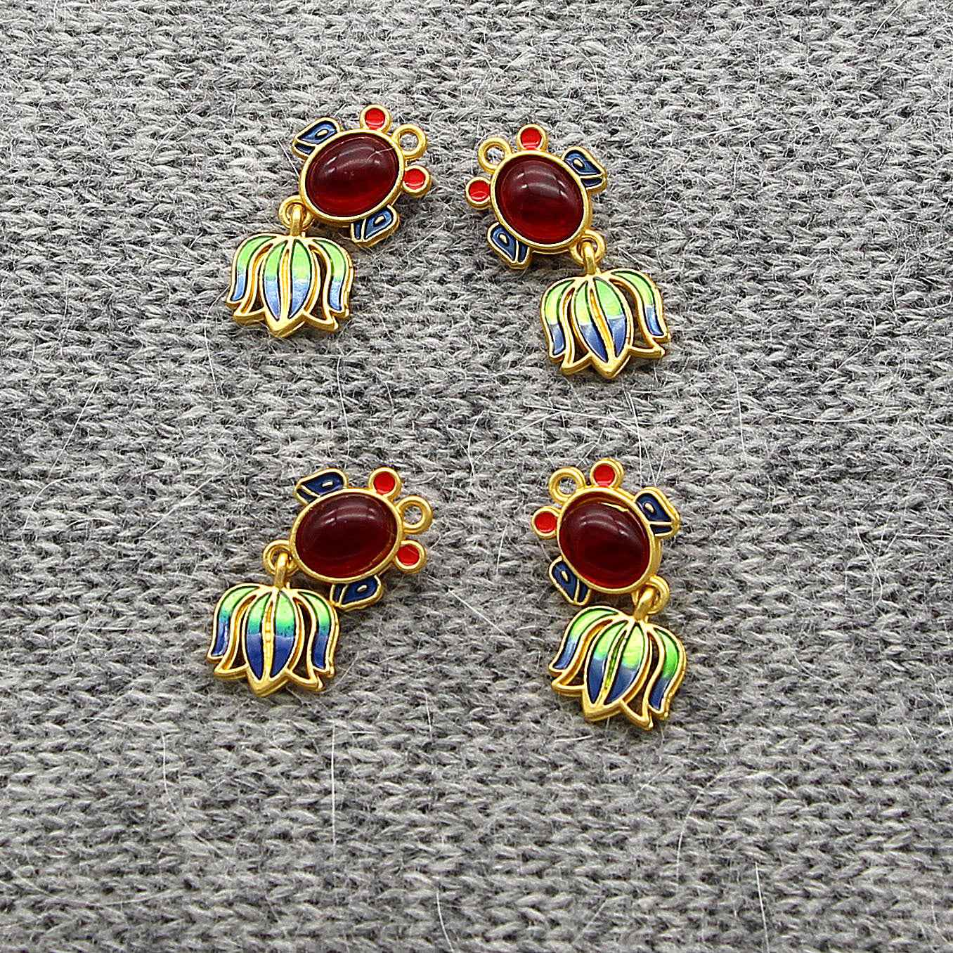 Four goldfish-shaped metal buttons with glossy red oval centers on grey fabric