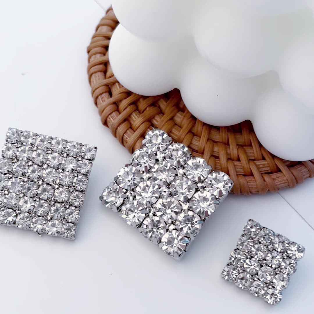 Silver diamond-cut square rhinestone metal button, held in hand
