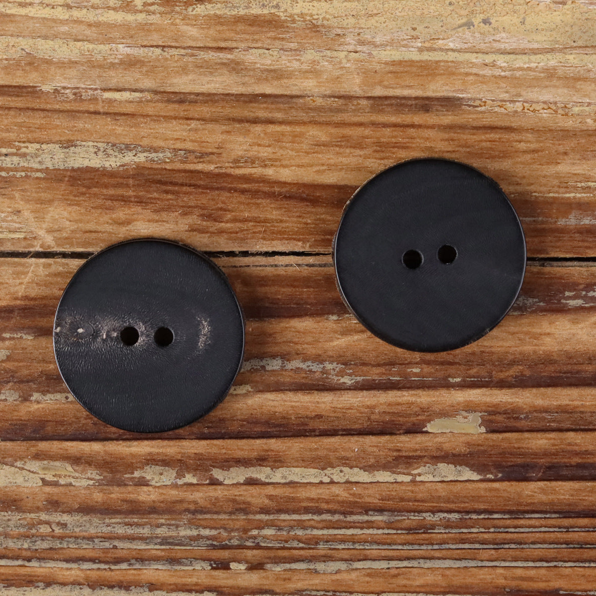 Round dark button with two holes, distressed matte finish