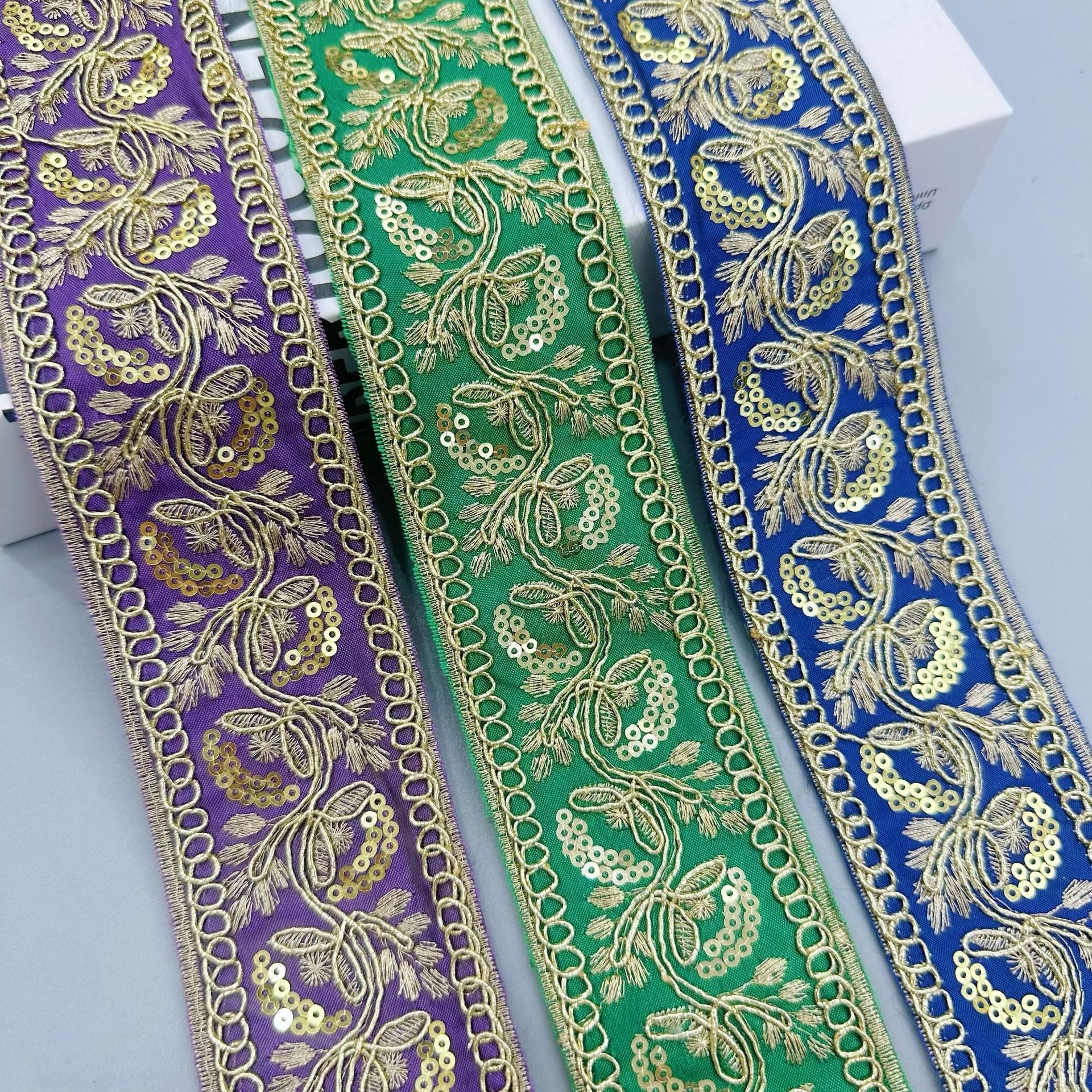 Gold sequin embroidered lace trim ribbon on purple, green, and blue fabrics with chain edge