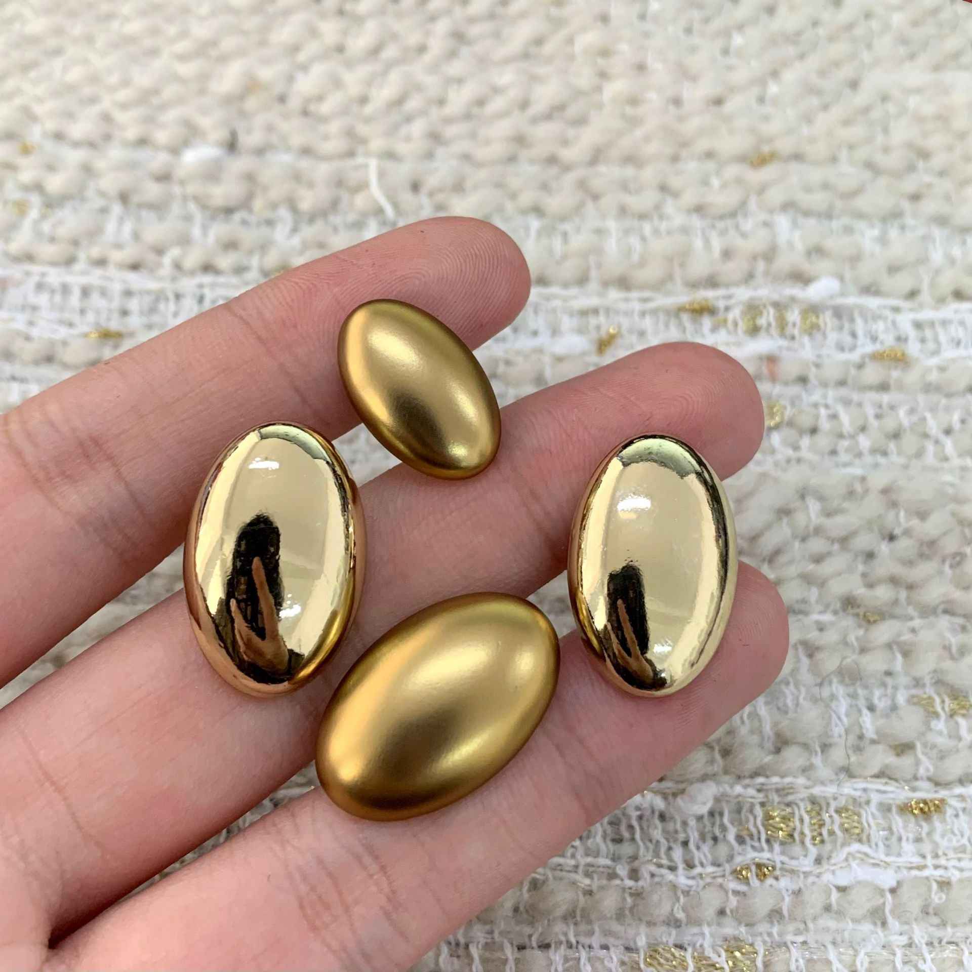 Assorted oval gold alloy shank buttons on hand, glossy domed fronts