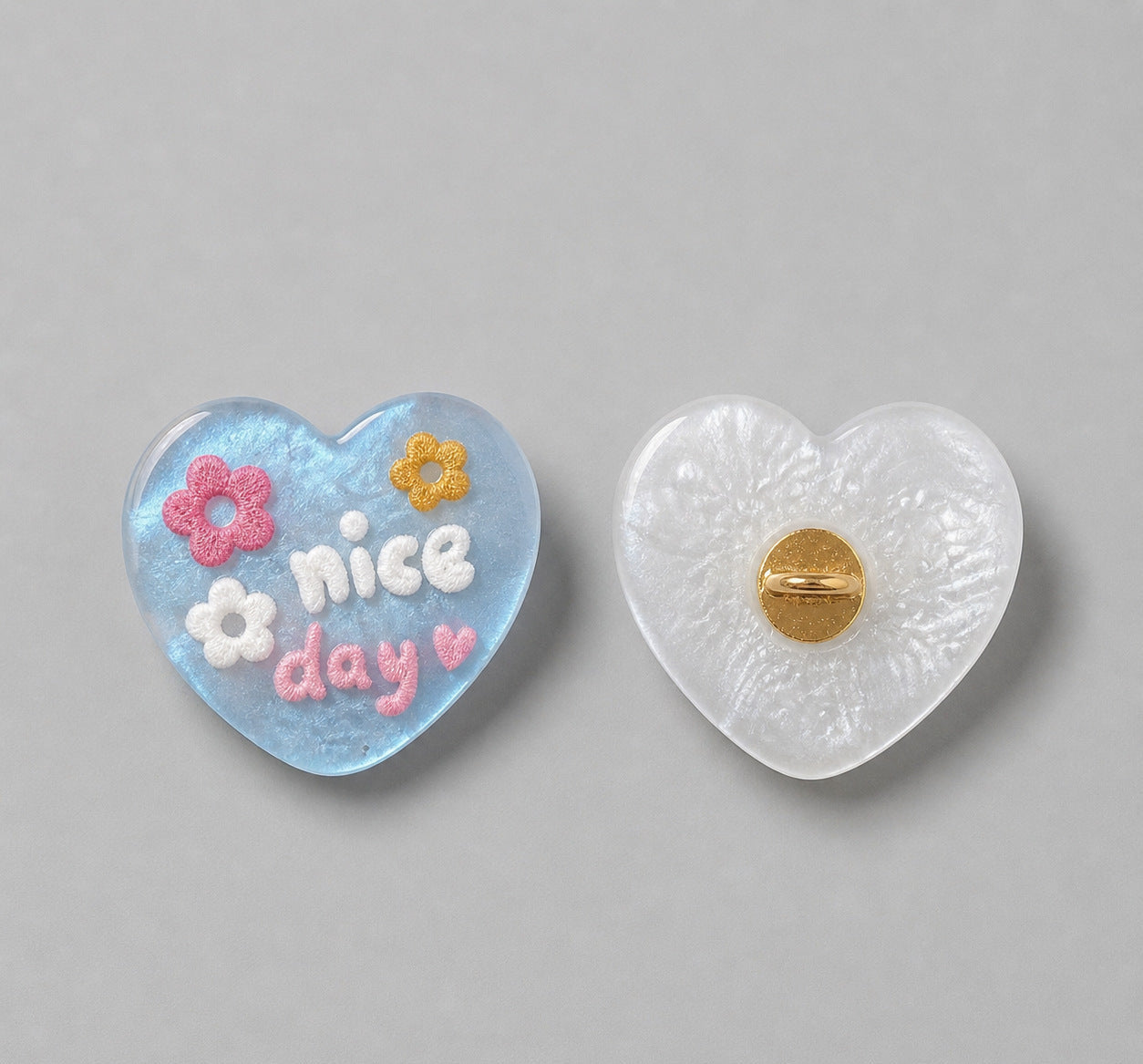 Light blue heart-shaped resin button with “nice day” and flowers; white back with gold pin