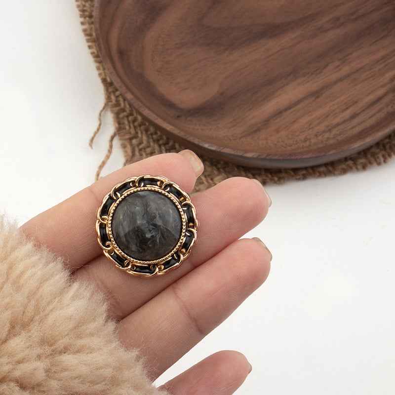 Black resin shank button with gold-tone ornate ring edge
