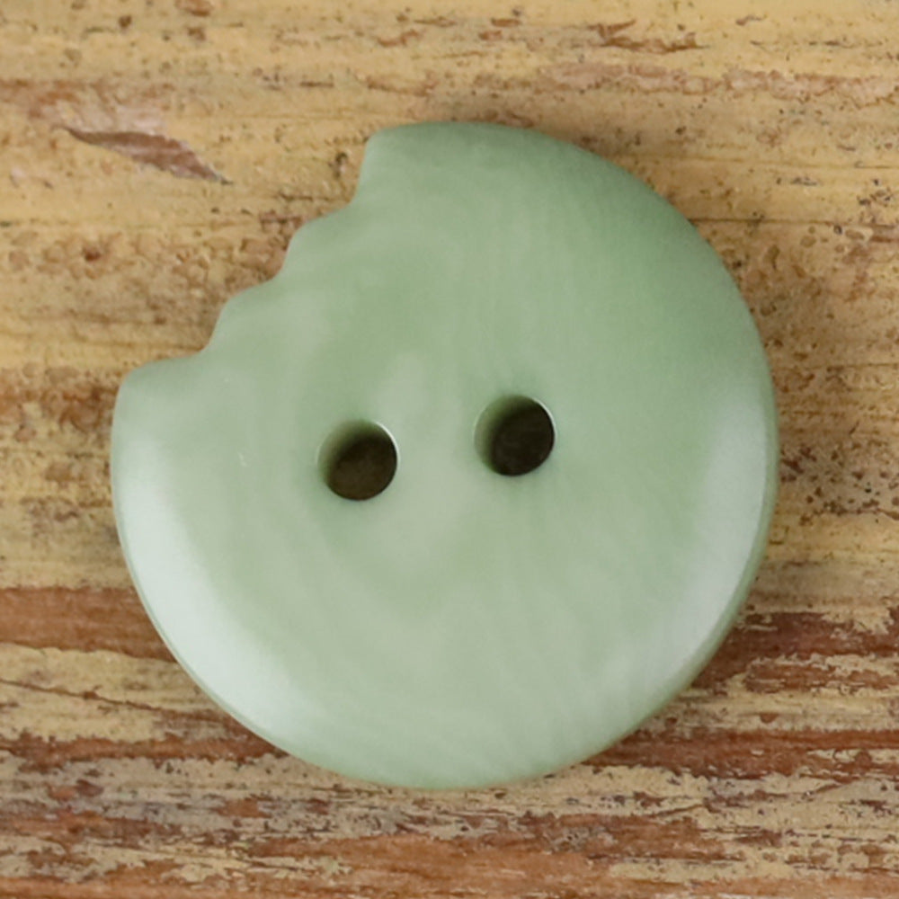 Light green irregular seed button with two holes and a scalloped edge.