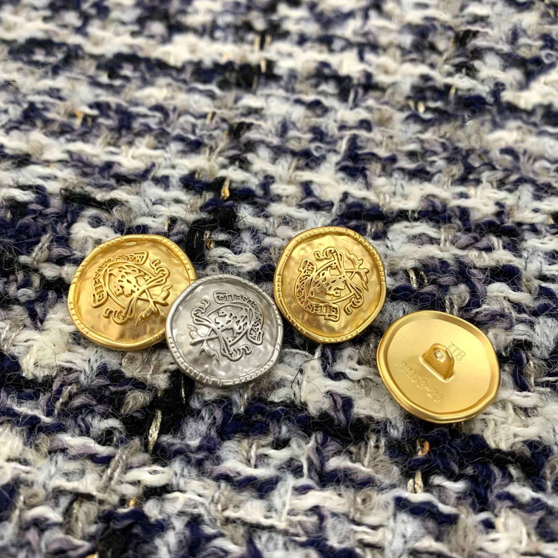 Goldfarbige Rundknöpfe aus Metall mit Öse, erhabenes Wappen-Design auf der Vorderseite.