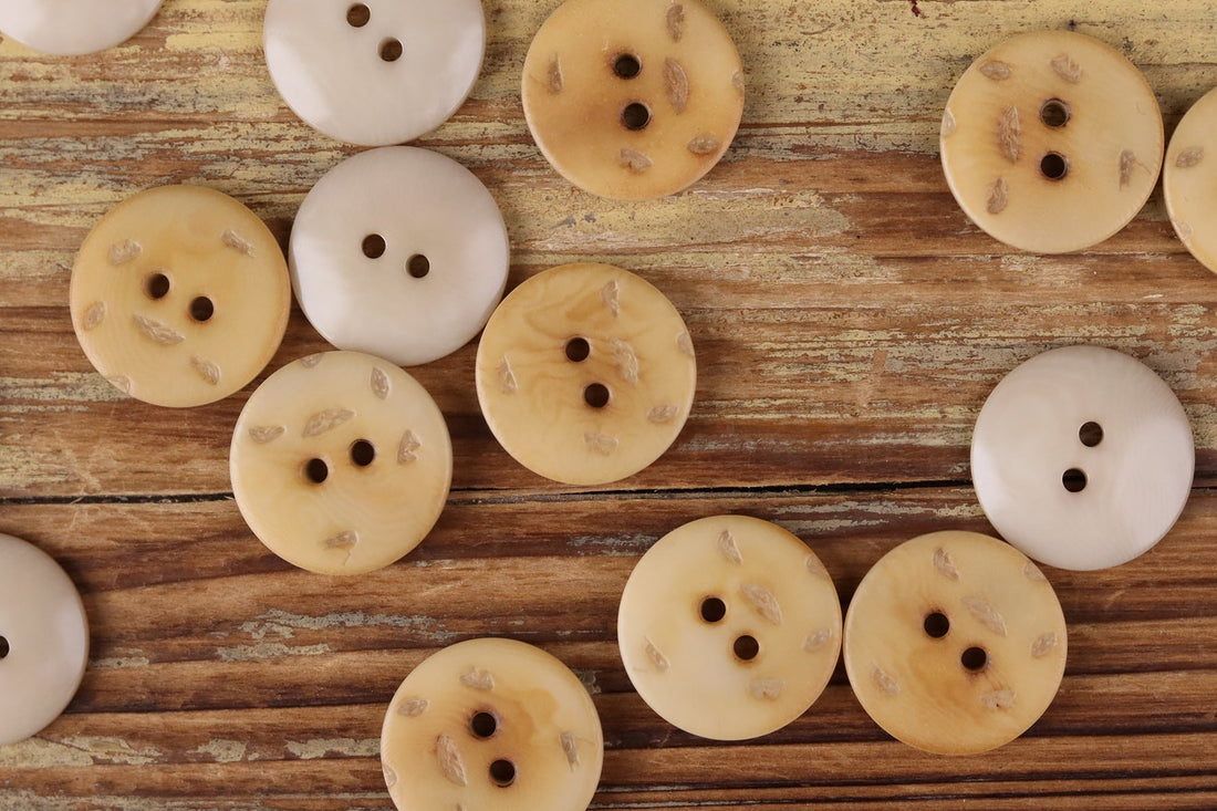 Round 2-hole buttons in pale cream and light golden tones with small printed marks