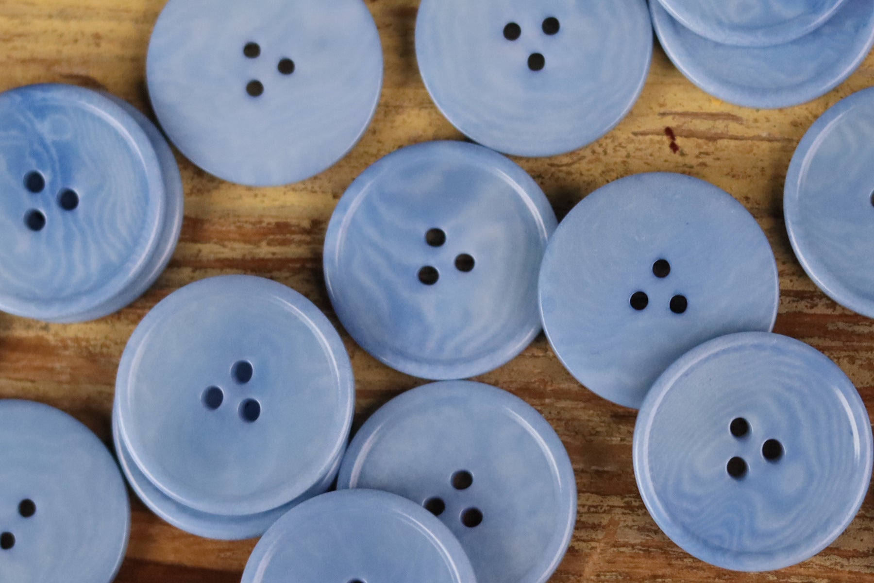 Assorted light blue round 3-hole buttons with thin rim on wood