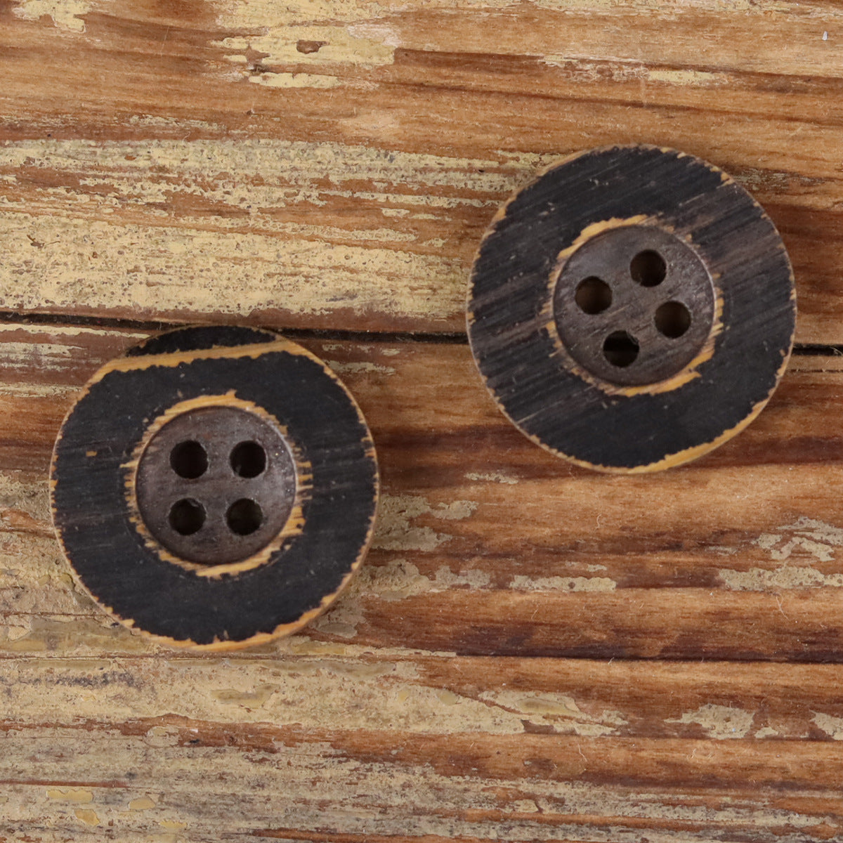Two round black distressed wood buttons with four holes on a wooden surface.