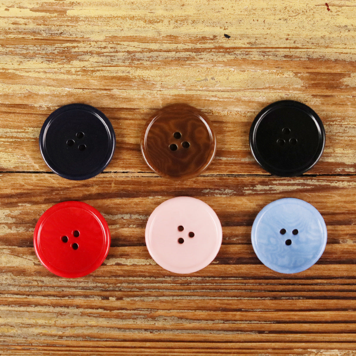 Round 3-hole buttons: black, brown, red, light pink, and light blue on wood