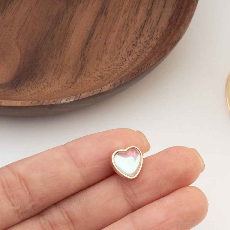 Heart-shaped button with white iridescent center and gold-tone edge, close-up on hand