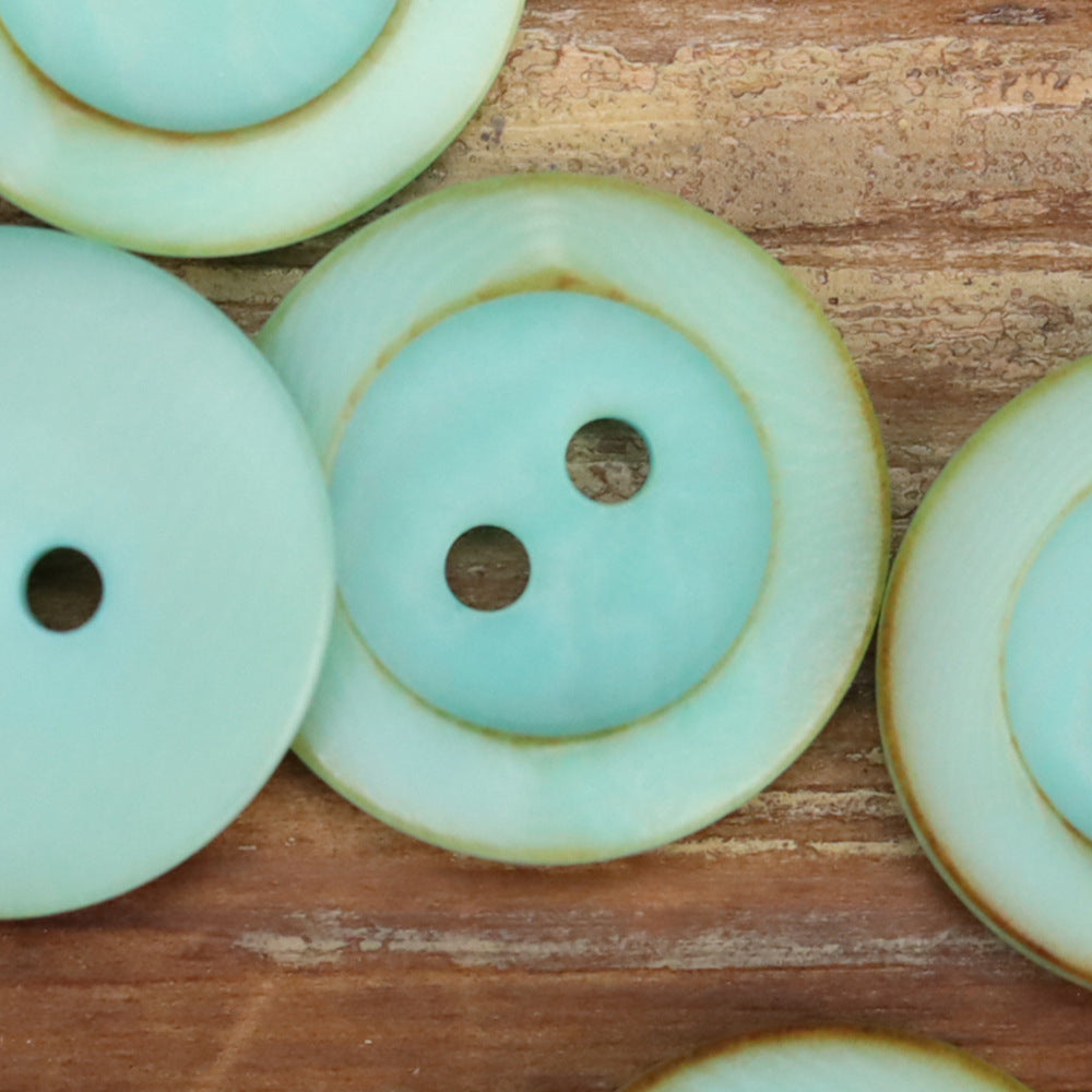 Turquoise round 2-hole button close-up with scorched rim edge and textured finish