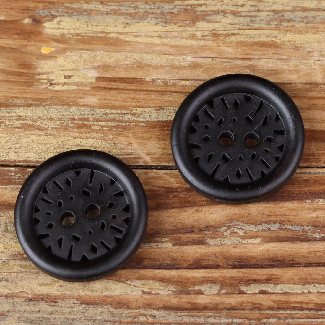 Round dark 2-hole coat button with laser-cut radial design and smooth rim