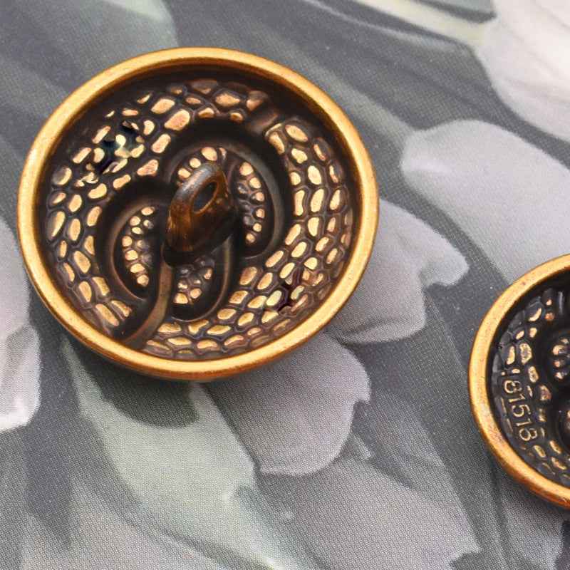 Round antique metal coat button with shank, dotted texture, and swirl front detail