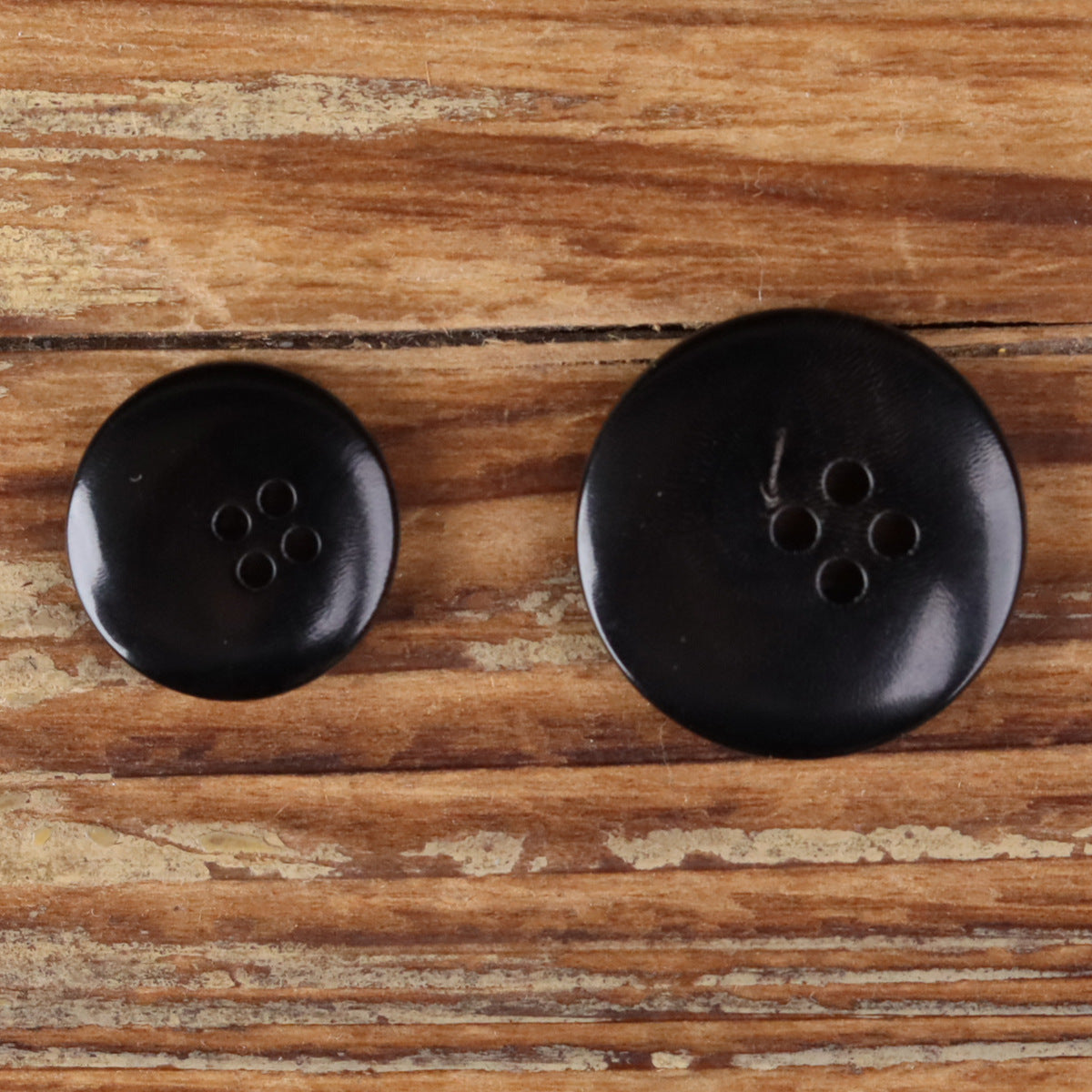Two black 4-hole round buttons with visible shank holes