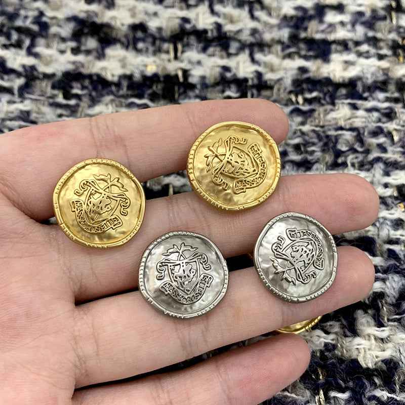 Verschiedene gold- und silberfarbene Metallknöpfe in einer Hand, Rundform mit Wappenmotiv.