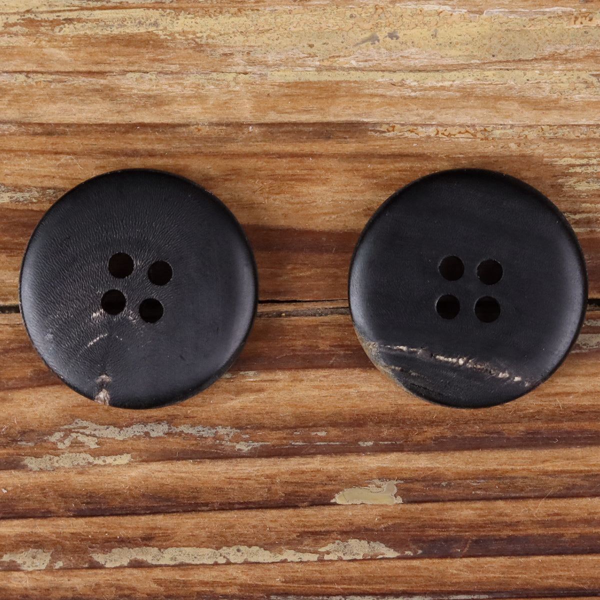 Two dark round 4-hole horn buttons with smooth matte finish