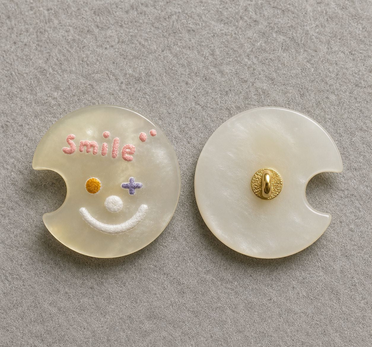 Beige moon-shaped resin shank button with colorful smiley face; gold back shank detail