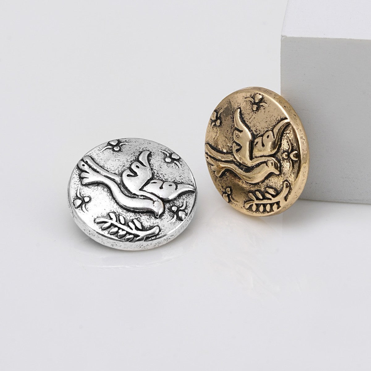 Pair of embossed metal shank buttons: one silver, one gold, flying bird design