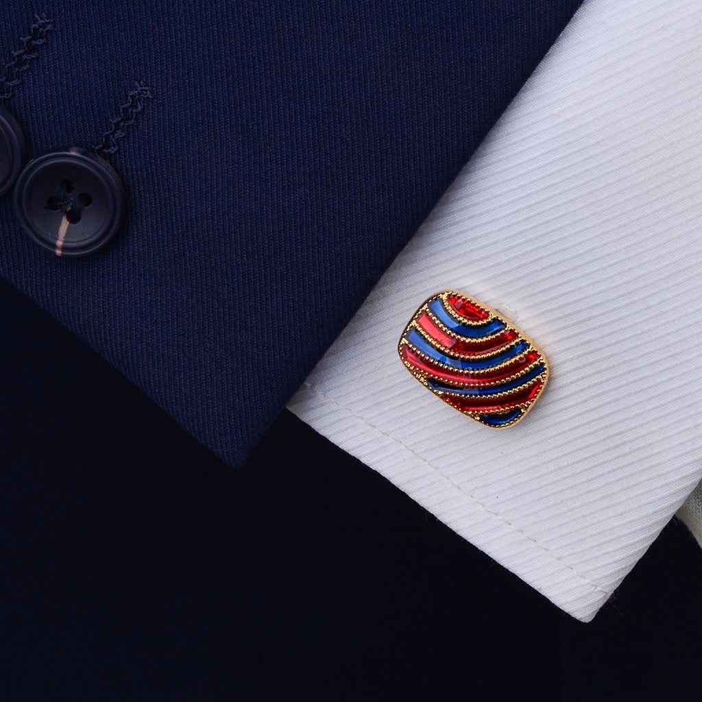 Gold oval cuff link with red and blue striped enamel on a white shirt cuff